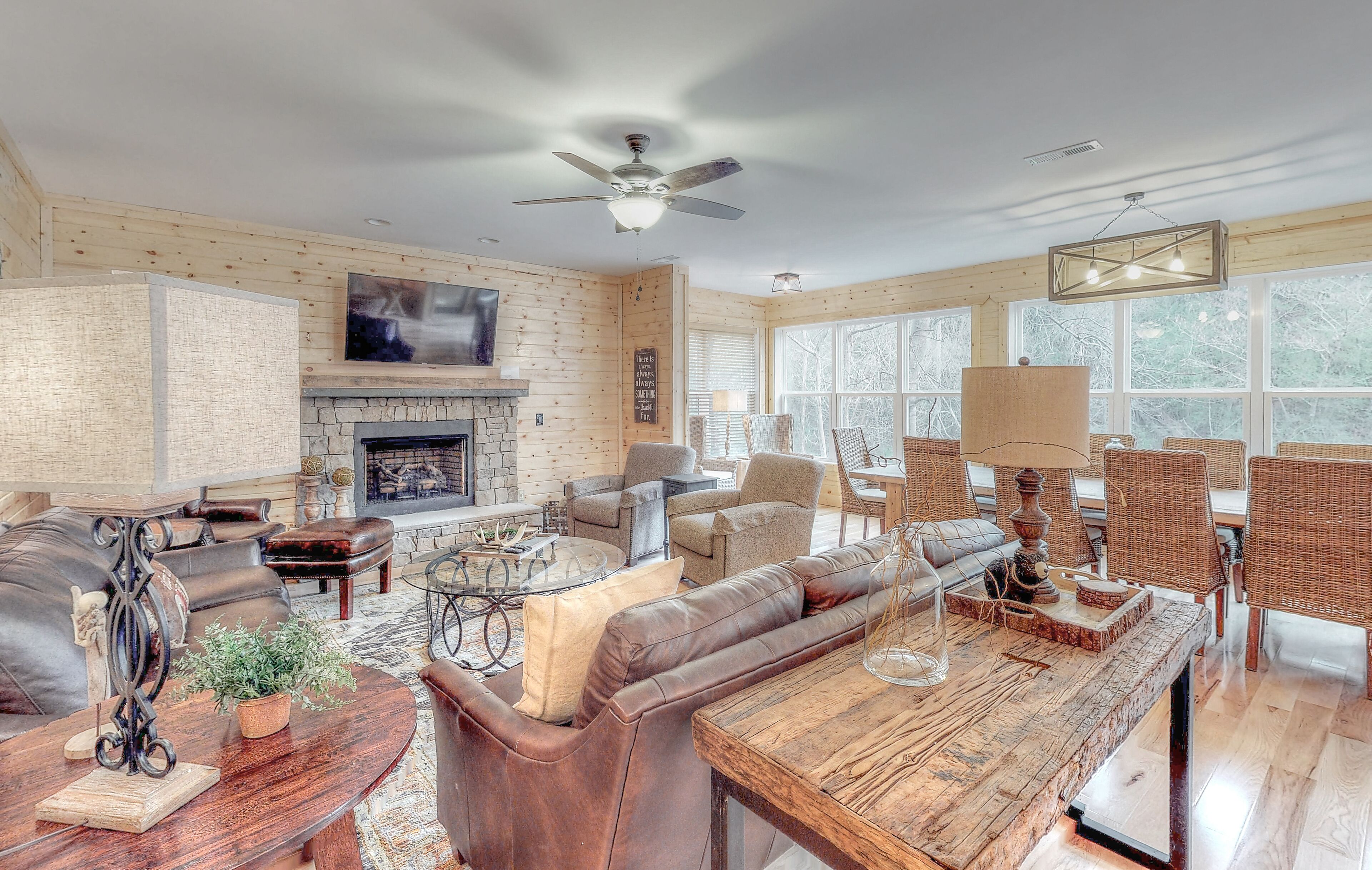 A spacious living room with a fireplace, leather furniture, wicker chairs, and a large window with a view of trees.