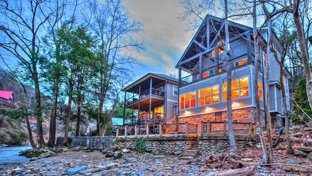 A two-story house with a stone foundation, wooden deck, and large windows.