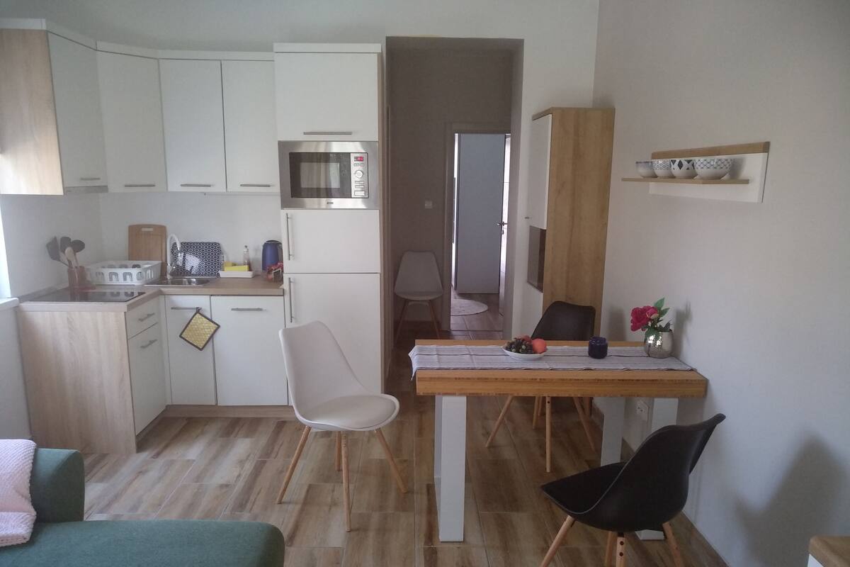 Una cocina compacta con armarios blancos, un microondas y una zona de comedor con una mesa y dos sillas.