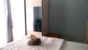 Camera d'albergo con un letto, uno specchio, un piccolo comodino in legno e una sedia blu visibile nel riflesso.