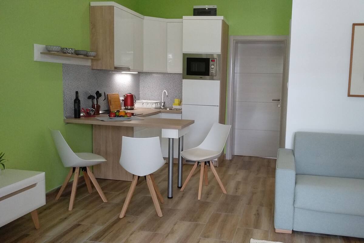 Un espacio habitable compacto con kitchenette, un área de comedor con dos sillas, un sofá y un cuadro en la pared.