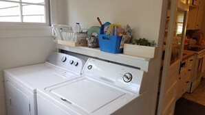 Un espace buanderie équipé d’un lave-linge et d’un sèche-linge à chargement frontal, d’une étagère contenant des produits de nettoyage et d’une fenêtre laissant entrer la lumière naturelle.