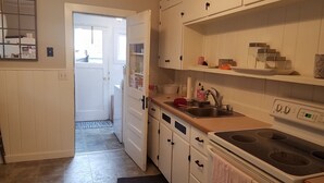 Une cuisine avec des meubles blancs, un évier et une cuisinière. Une porte donne accès à une autre pièce.