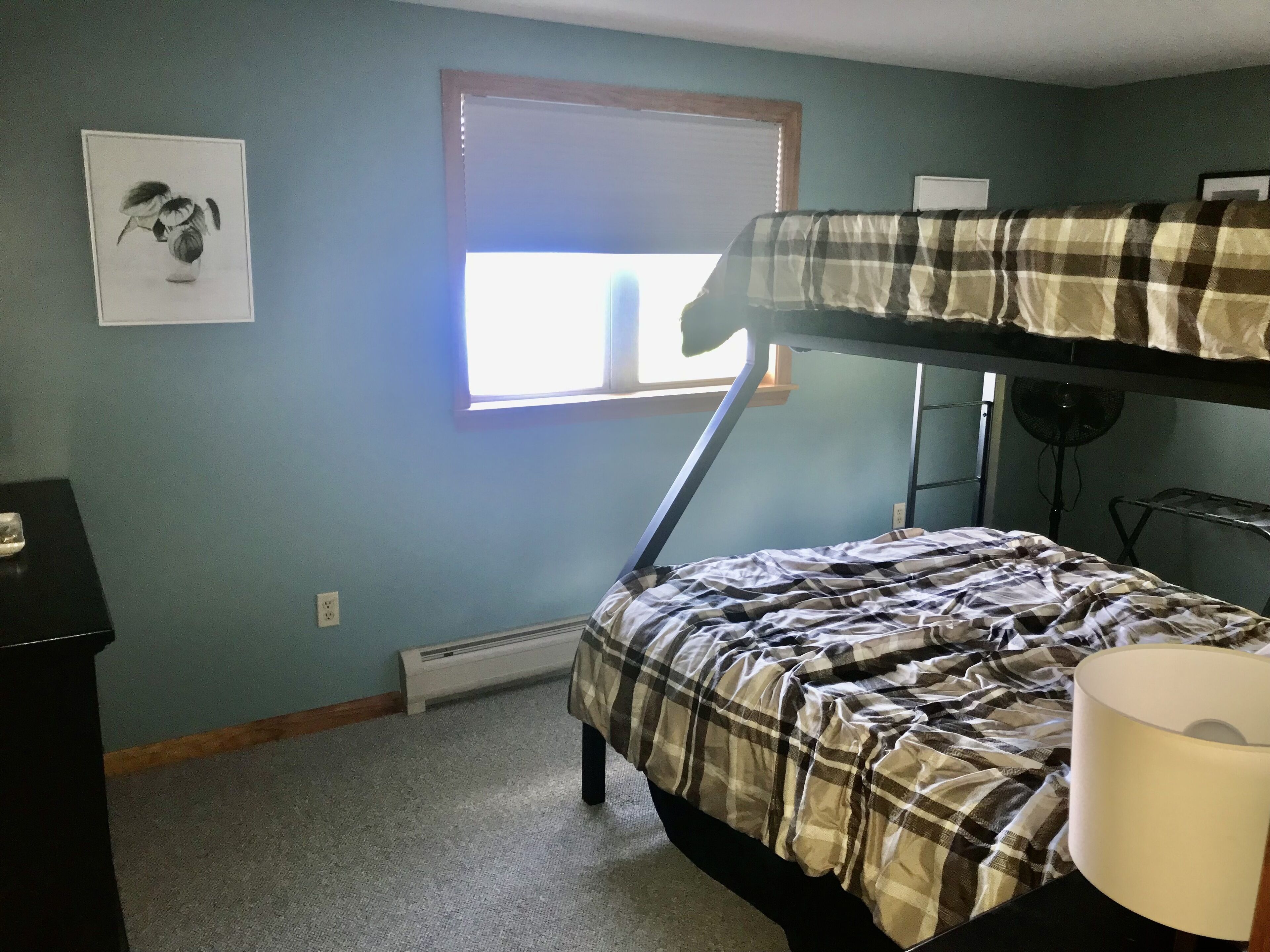 A bedroom with a bunk bed, a window, a radiator, a desk, and a lamp.