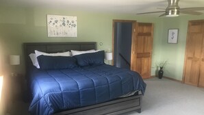 Un dormitorio con cama, ventilador de techo, mesita de noche, lámpara y puerta.