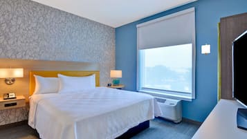 Quarto de hotel com uma cama grande, mesa de cabeceira com abajur, janela com vista e televisão sobre um suporte.