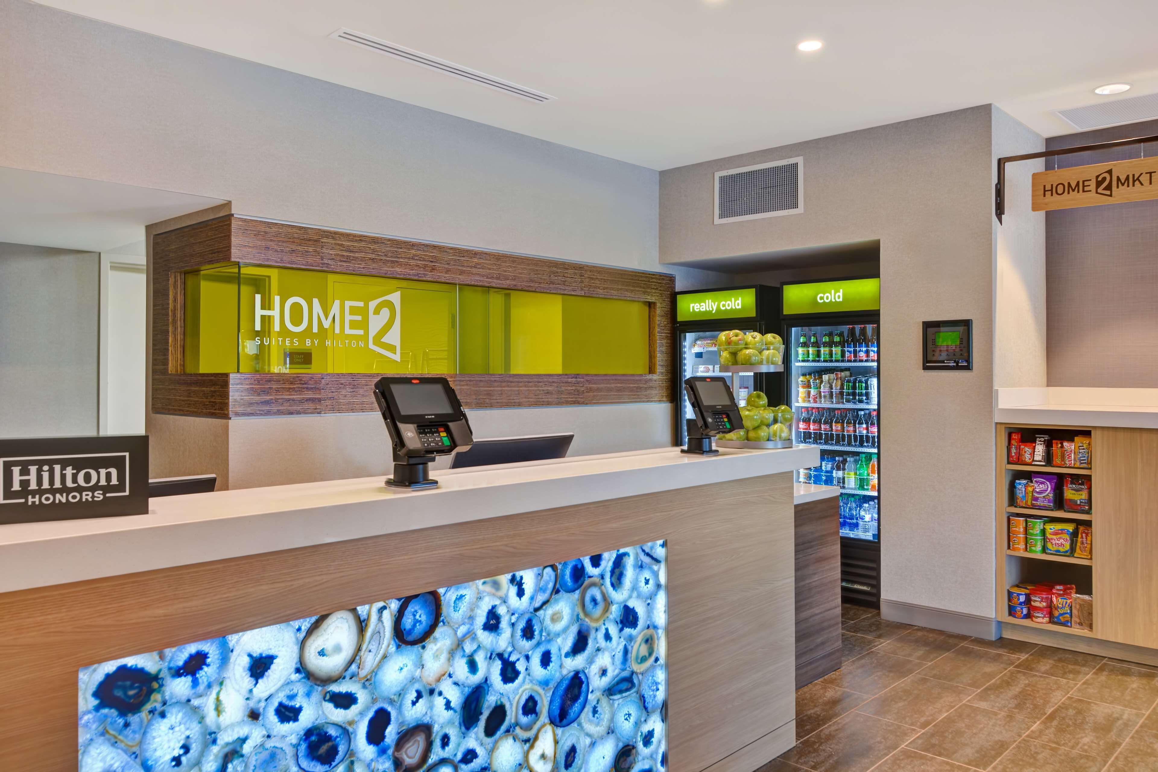 Ein Hotel-Empfangsbereich mit modernem Design, inklusive einer Rezeption, einem digitalen Display, einem Getränkekühler und einer Selbstbedienungs-Speiseausgabe.