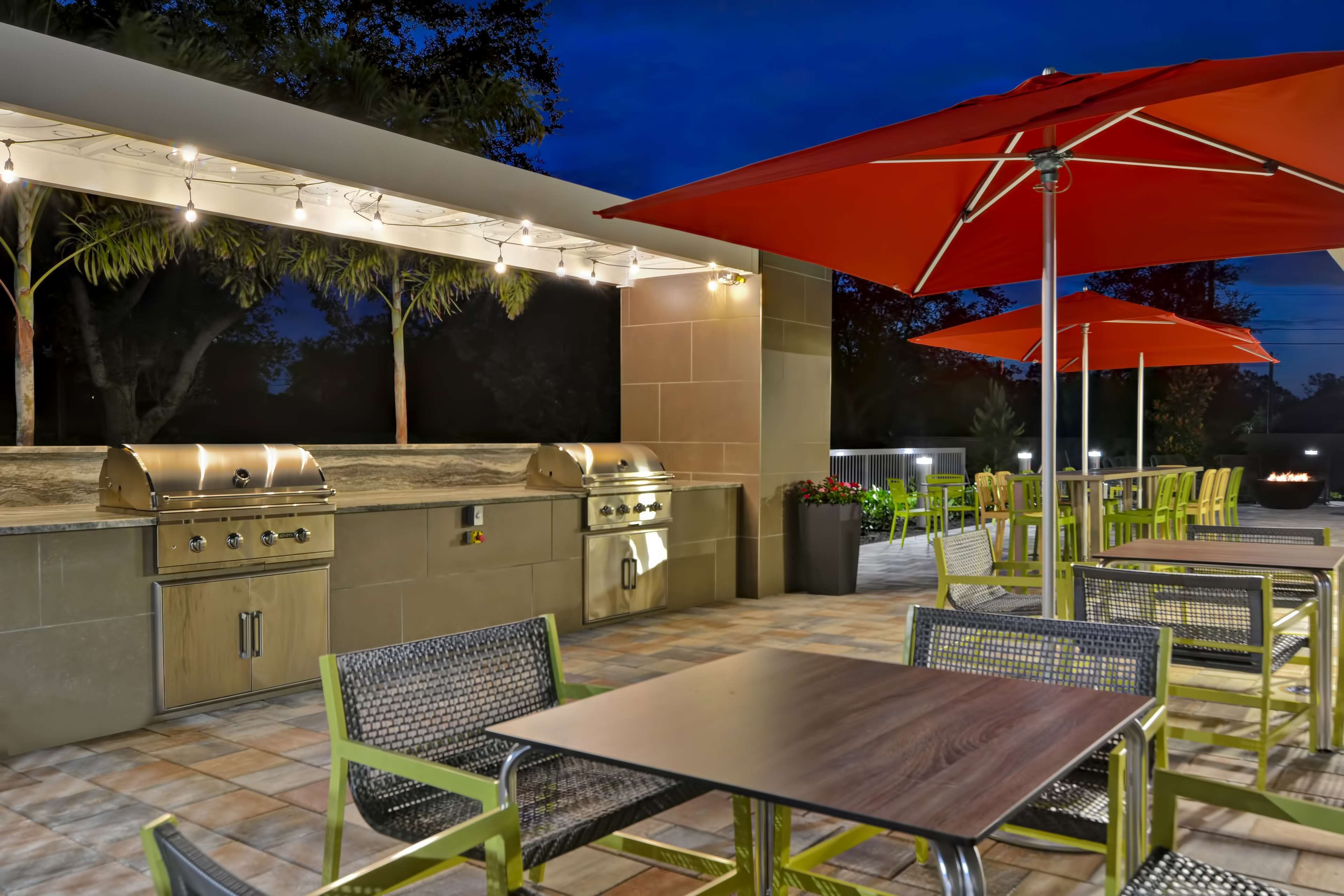 An outdoor patio with a grill, tables, chairs, and red umbrellas.