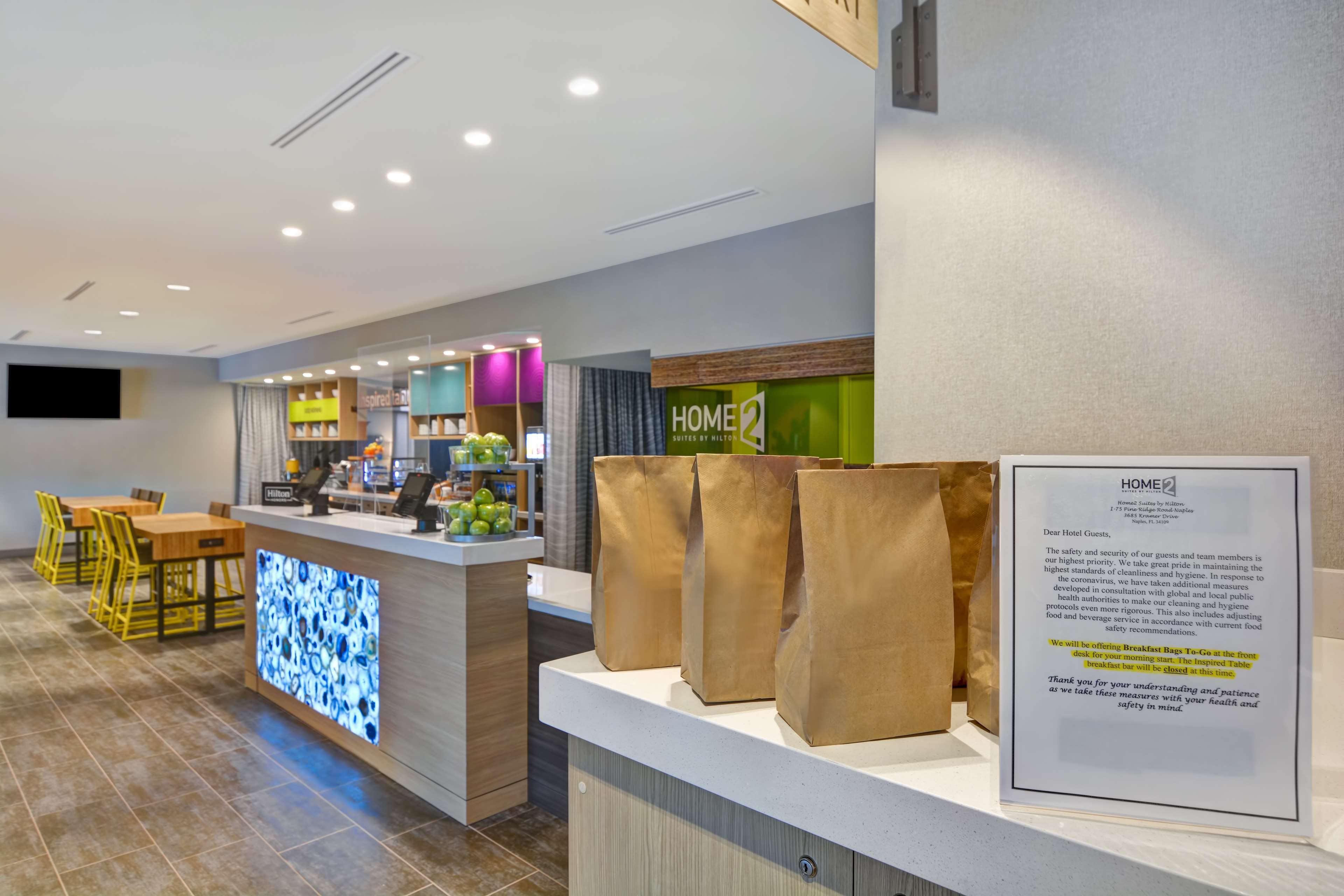 A hotel reception area with a counter, seating area, and a sign indicating 'HOME2' suites by Hilton.