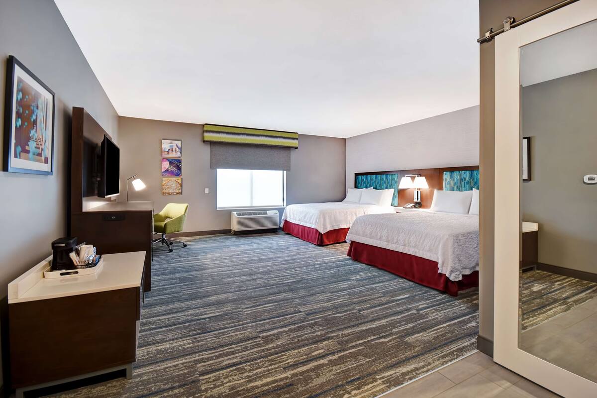 A hotel room with two beds, a desk, a chair, a TV, and a window with a view.
