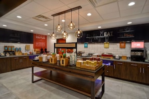 A breakfast area with a wooden table, hanging lights, and various food items displayed on the counter. - Hampton Inn Pleasant View, TN (Pleasant View)