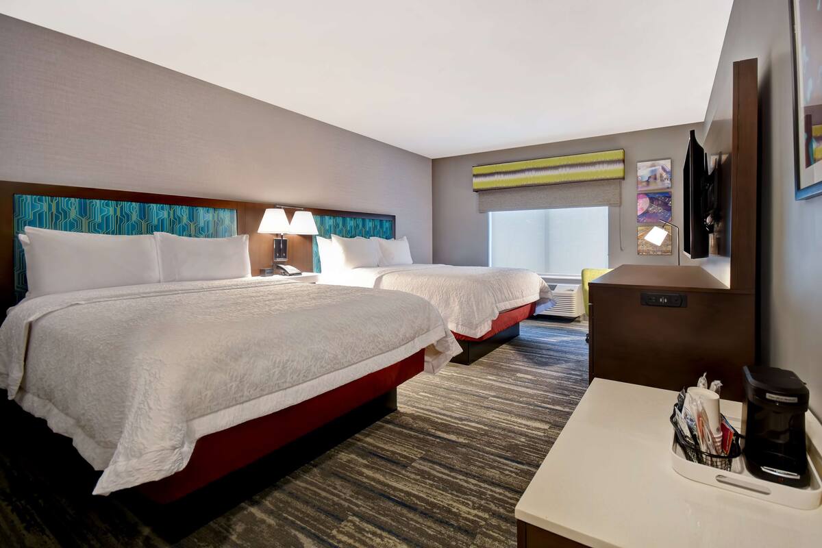 A hotel room with two beds, a desk with a coffee maker, and a TV mounted on the wall.