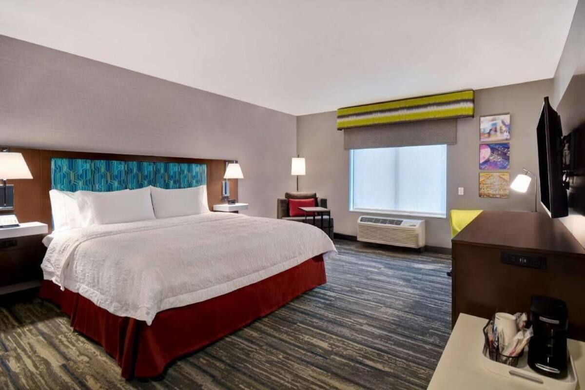 A hotel room with a bed, bedside tables, a desk, a chair, a TV, and a window.