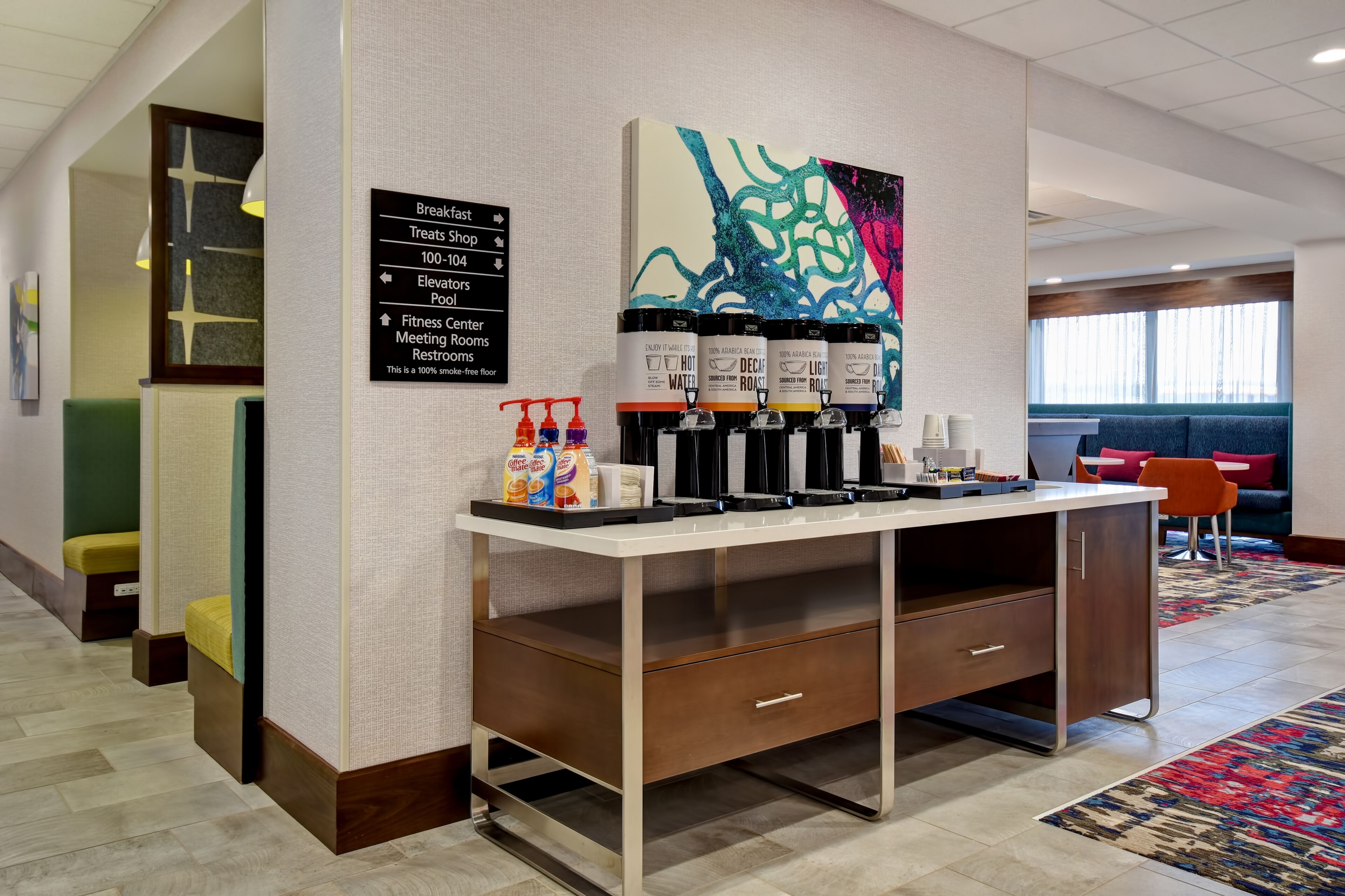 Un vestíbulo de hotel con estación de café, zona de estar y señalización.