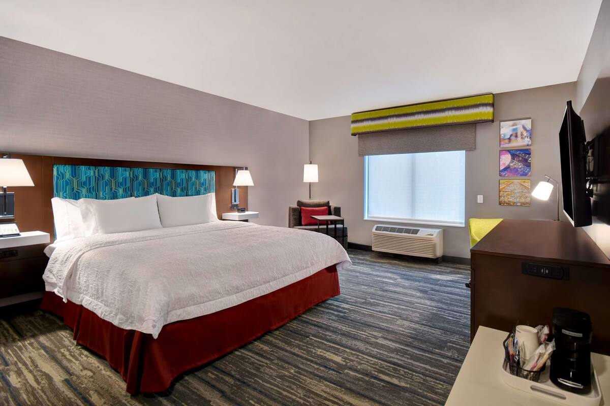 A hotel room with a large bed, a desk with a coffee maker, a TV, and a window with a view.