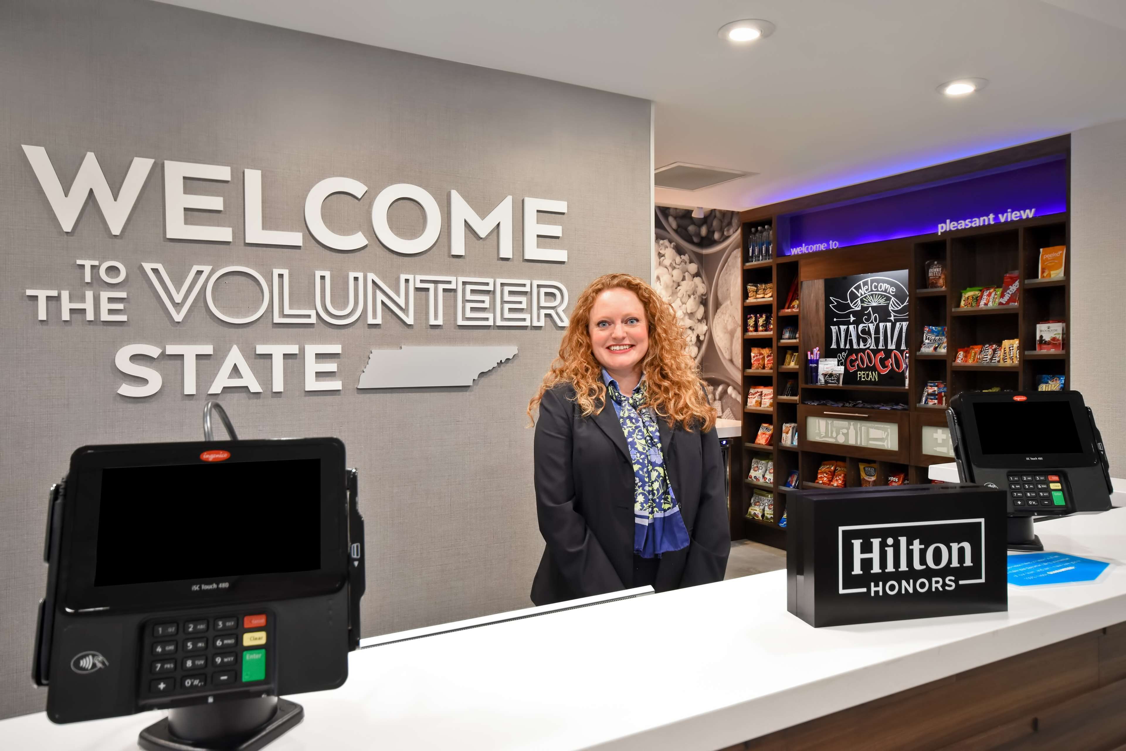 A reception area with a 'Welcome to the Volunteer State' sign, a Hilton Honors sign, and a self-service kiosk.