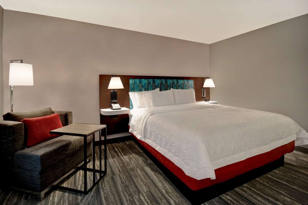 A hotel room with a large bed, a sofa, a small table, and two bedside lamps.