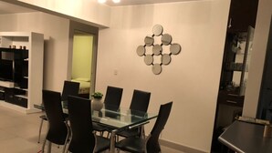 A modern dining area with a glass table and black chairs, a red stool, and a decorative wall piece. - Santa Maria del Mar, Terramar 315, 204 (Urb Santa Maria del Mar)