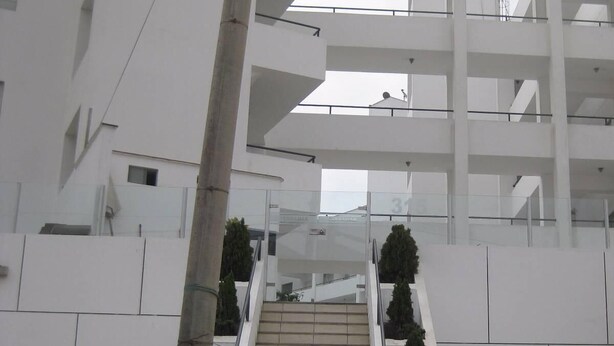A modern building with a central staircase leading to upper floors, surrounded by white walls and glass railings. - Santa Maria del Mar, Terramar 315, 204 (Urb Santa Maria del Mar)