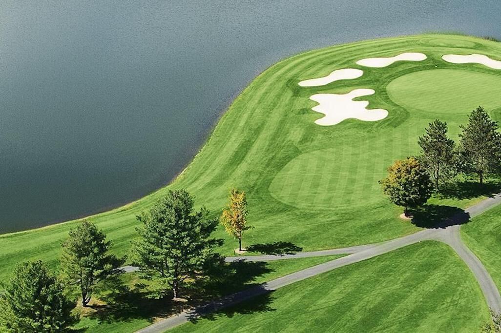 A golf course with a water body, trees, and a winding road.