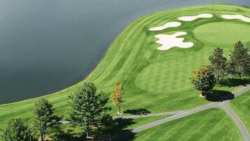 A golf course with a water body, trees, and a winding road.