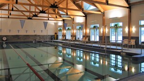 Piscina interior com pistas demarcadas, vigas de madeira e áreas de estar com plantas.