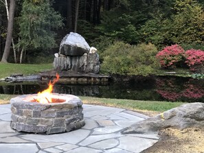 A stone fire pit with a fire burning in a garden setting. - Spacious home on picturesque grounds with stunning views.  Quechee - Woodstock  (Hartford)