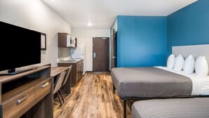 A hotel room with a bed, a desk, a television, a microwave, and a door. - WoodSpring Suites Bradenton (Bradenton)