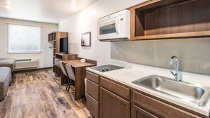 A compact kitchenette with a microwave, sink, and wooden cabinets. - WoodSpring Suites Bradenton (Bradenton)