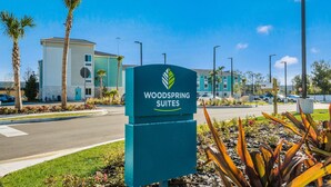 A sign for Woodspring Suites with a modern building in the background. - WoodSpring Suites Bradenton (Bradenton)
