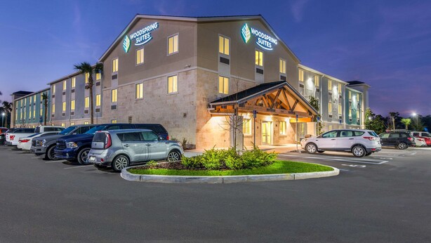 A hotel with a modern design, featuring a large parking lot and multiple vehicle types parked. - WoodSpring Suites Bradenton (Bradenton)