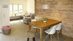 A dining area with a wooden table and white chairs, a wicker stool, and a hanging light fixture. - Wonderful private villa for 4 people with A/C, WIFI, TV and patio (Ullerst)