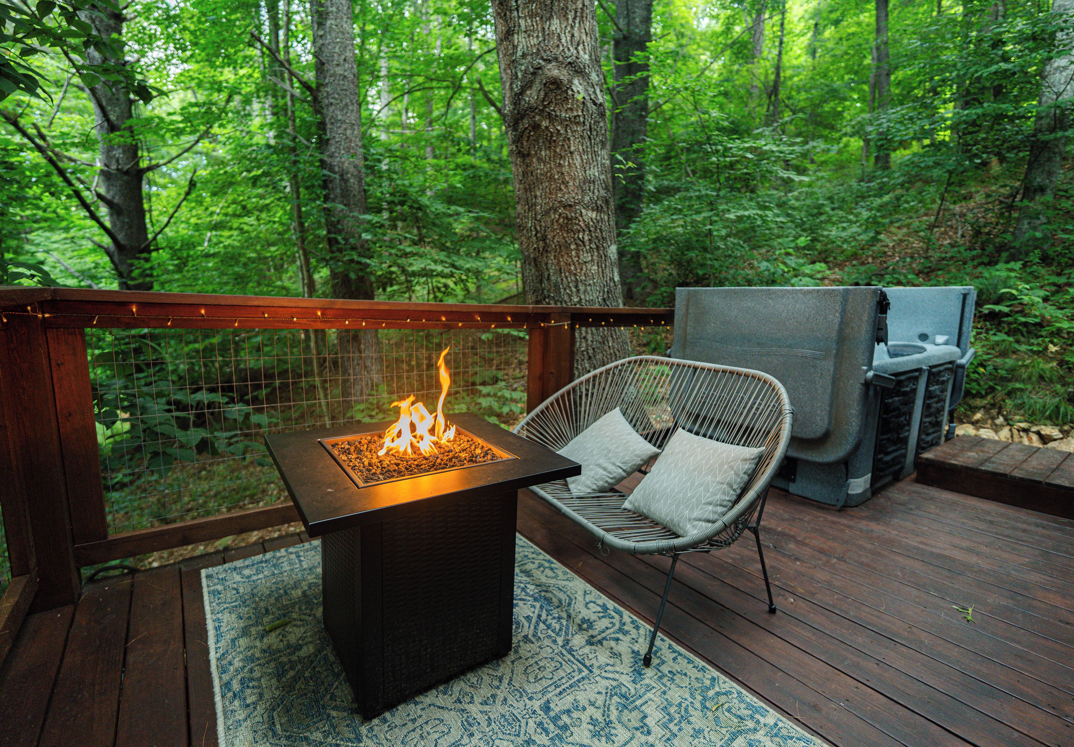 A deck with a square fire feature, a wicker chair with cushions, and a grill.