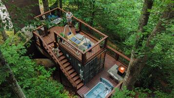 A wooden deck with a hot tub, outdoor seating, and a staircase leading to a deck area.