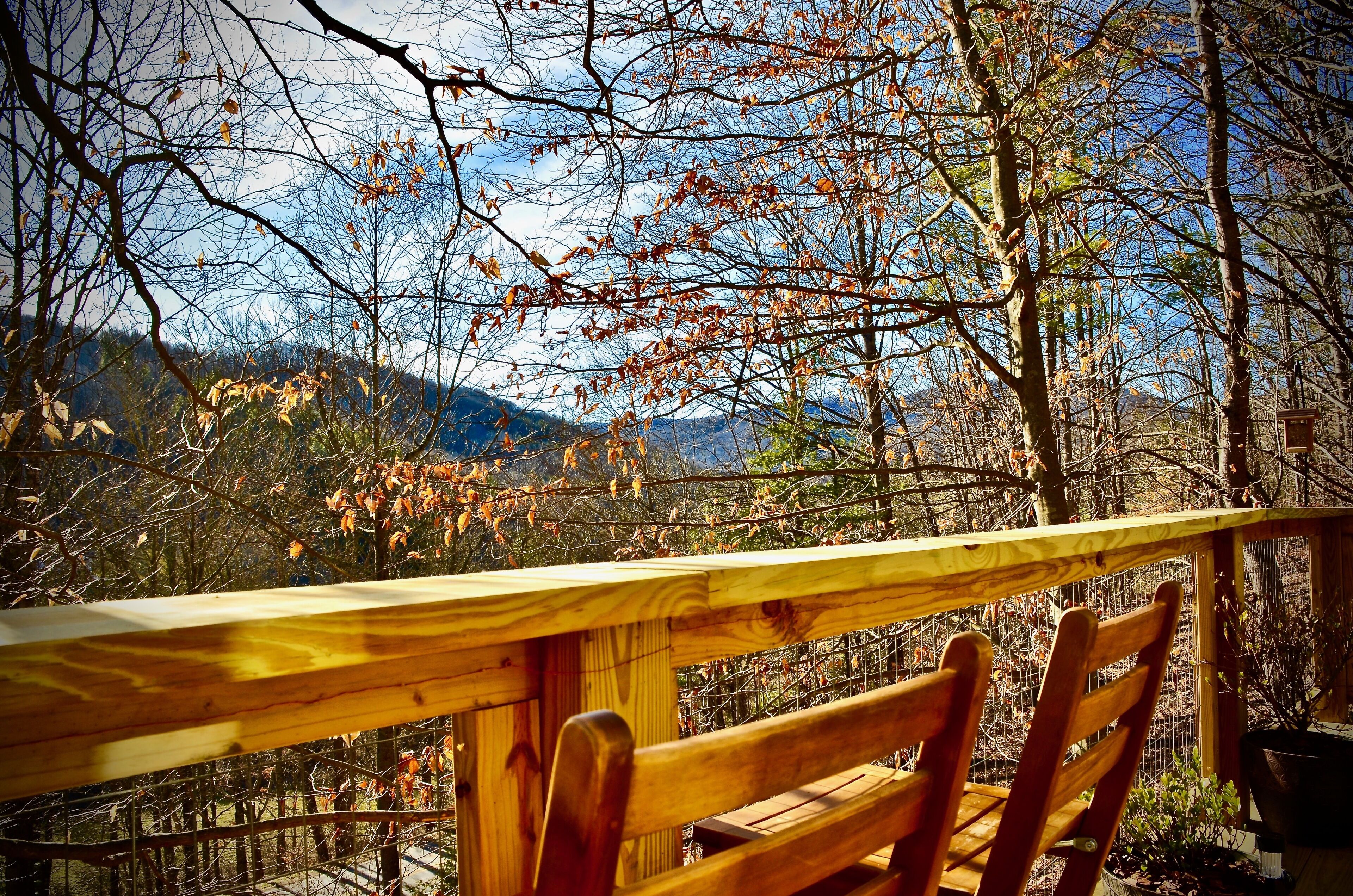 Eine Holzdar Terrasse mit Geländer mit Blick auf eine bewaldete Landschaft, Herbstlaub und entfernte Berge.