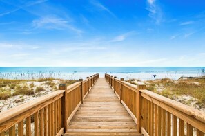 Ein hölzerner Steg führt zu einem Strand bei blauem Himmel.