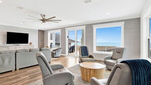 A spacious living room with a large TV, comfortable seating, a ceiling fan, and a view of the ocean through large windows. - Beachfront Luxury | Private Pool | Elevator (Gulf Shores)