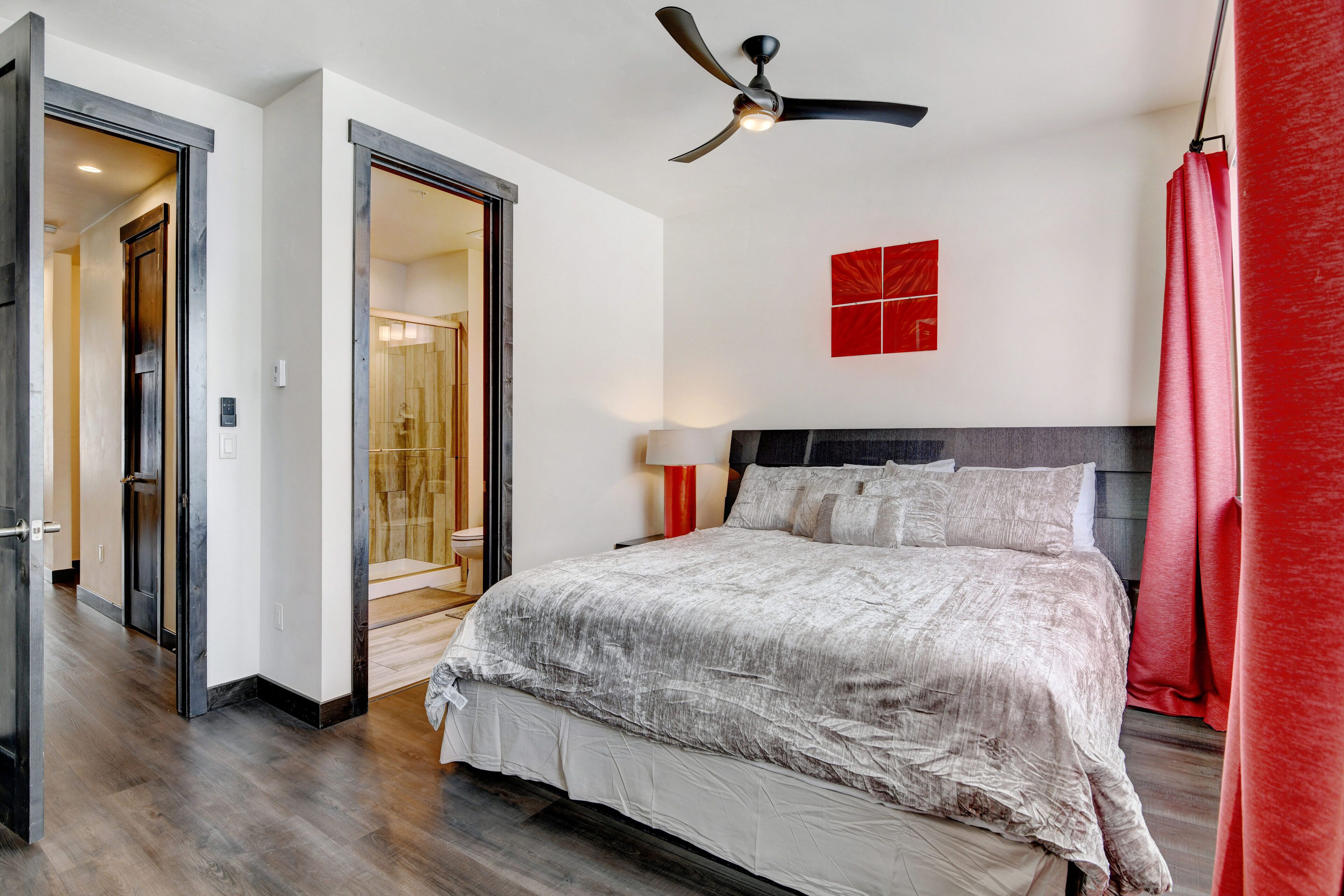 Un dormitorio moderno con una cama grande, un ventilador de techo y una pared de acento roja.