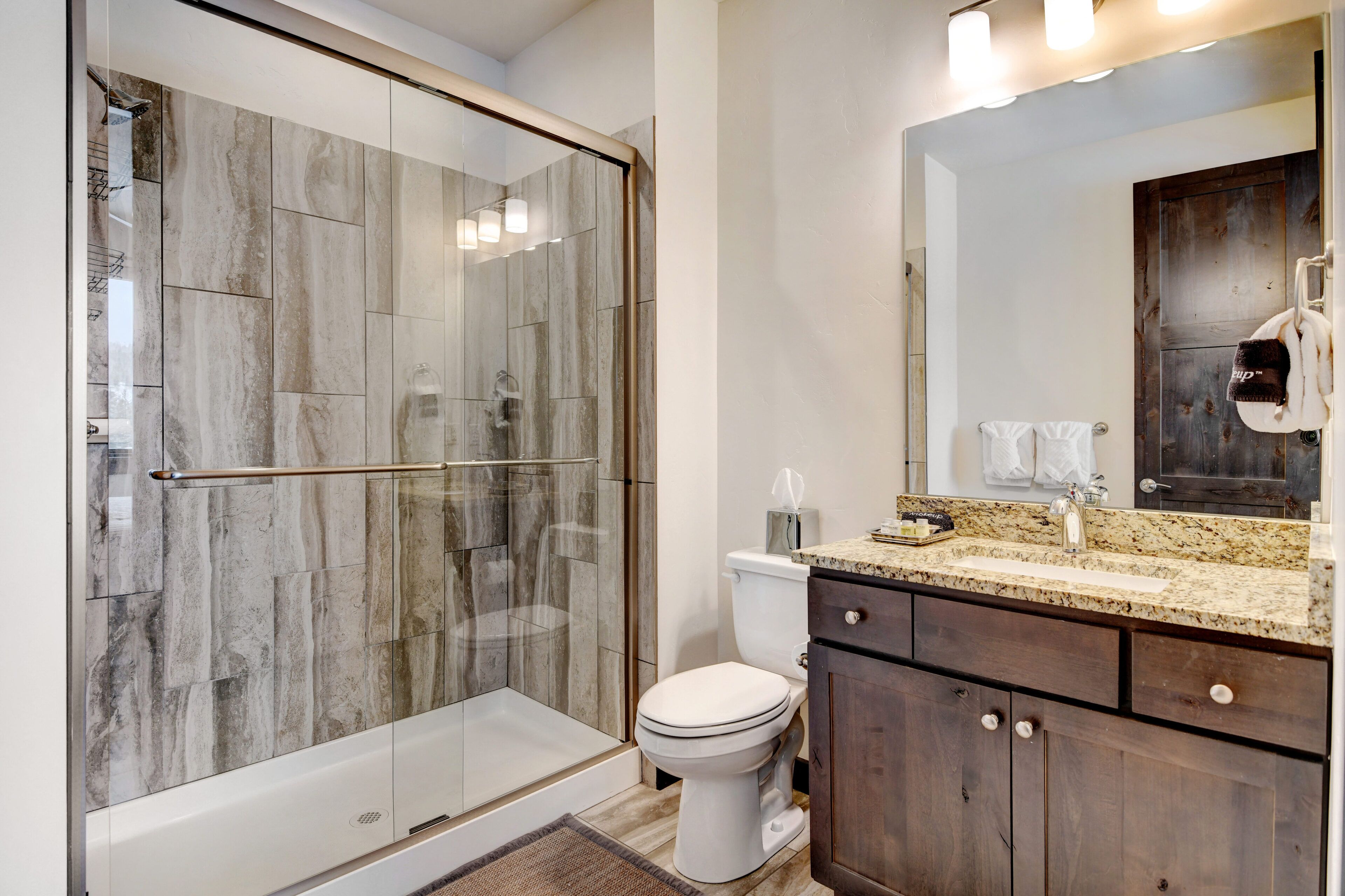 Un baño moderno con cabina de ducha de vidrio, inodoro blanco y lavamanos sobre encimera de granito.