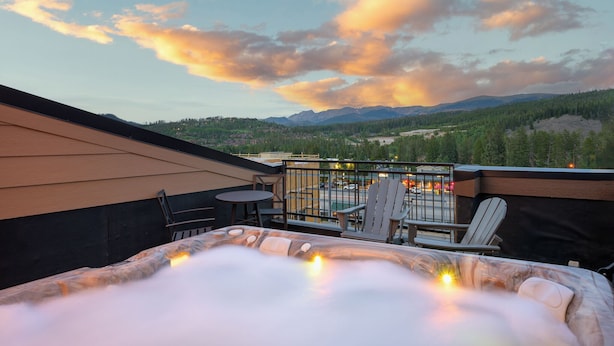 A rooftop terrace with a hot tub, seating area, and a view of mountains and trees.