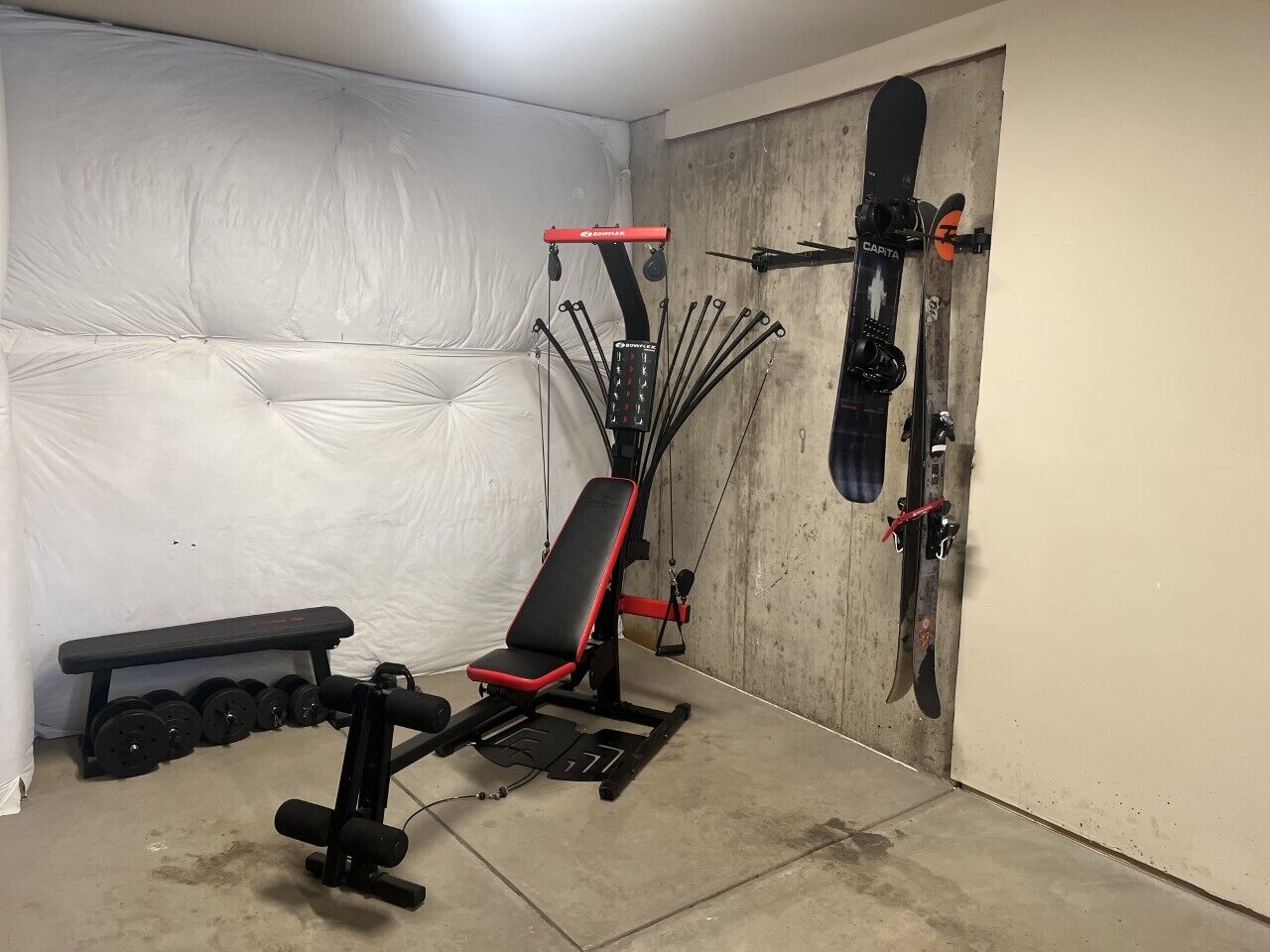 Un gimnasio con una banca, mancuernas, una estructura para sentadillas y esquíes montados en la pared.