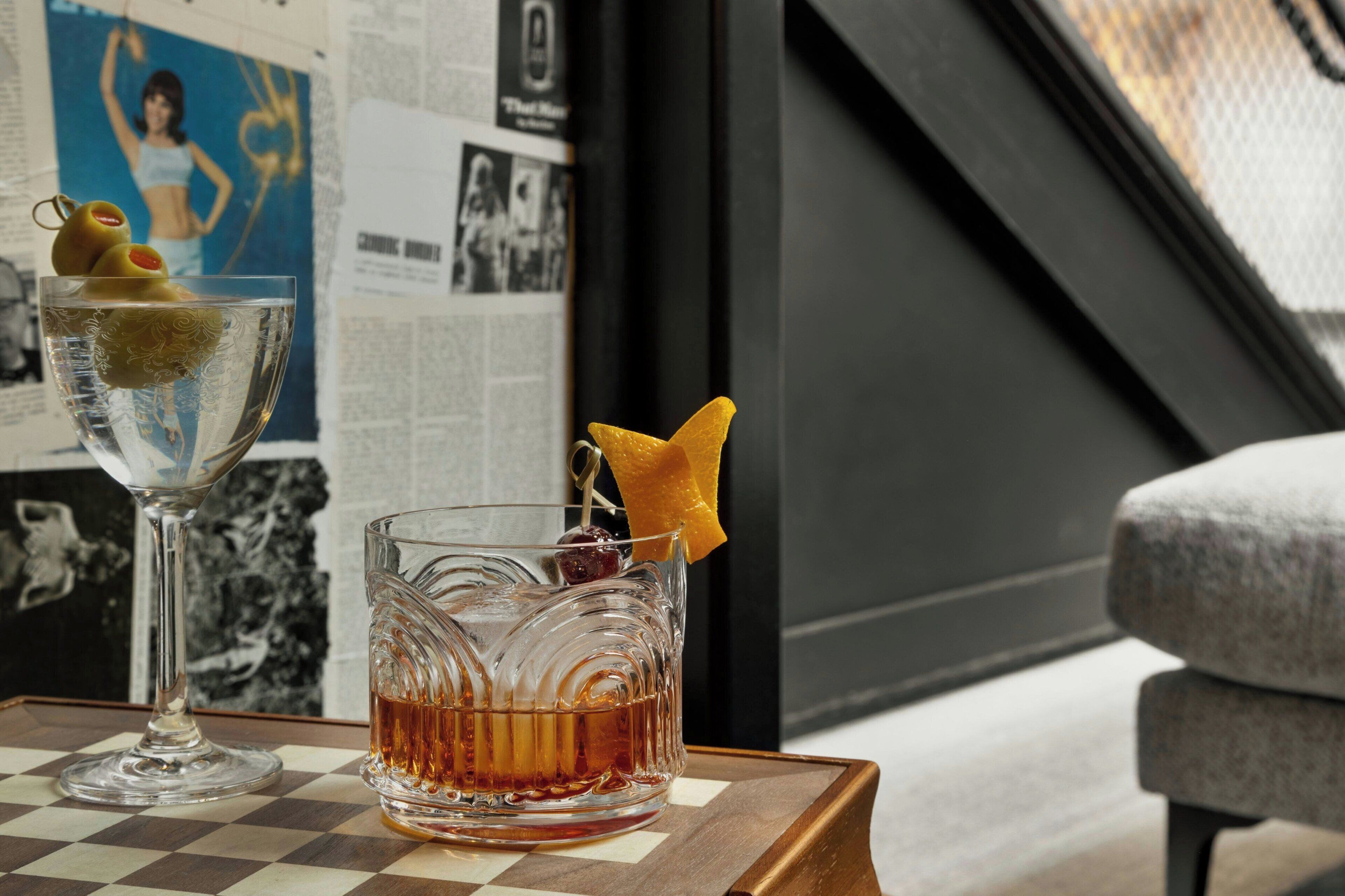 A bar area with a checkered table, two glasses of whiskey, and a poster on the wall.