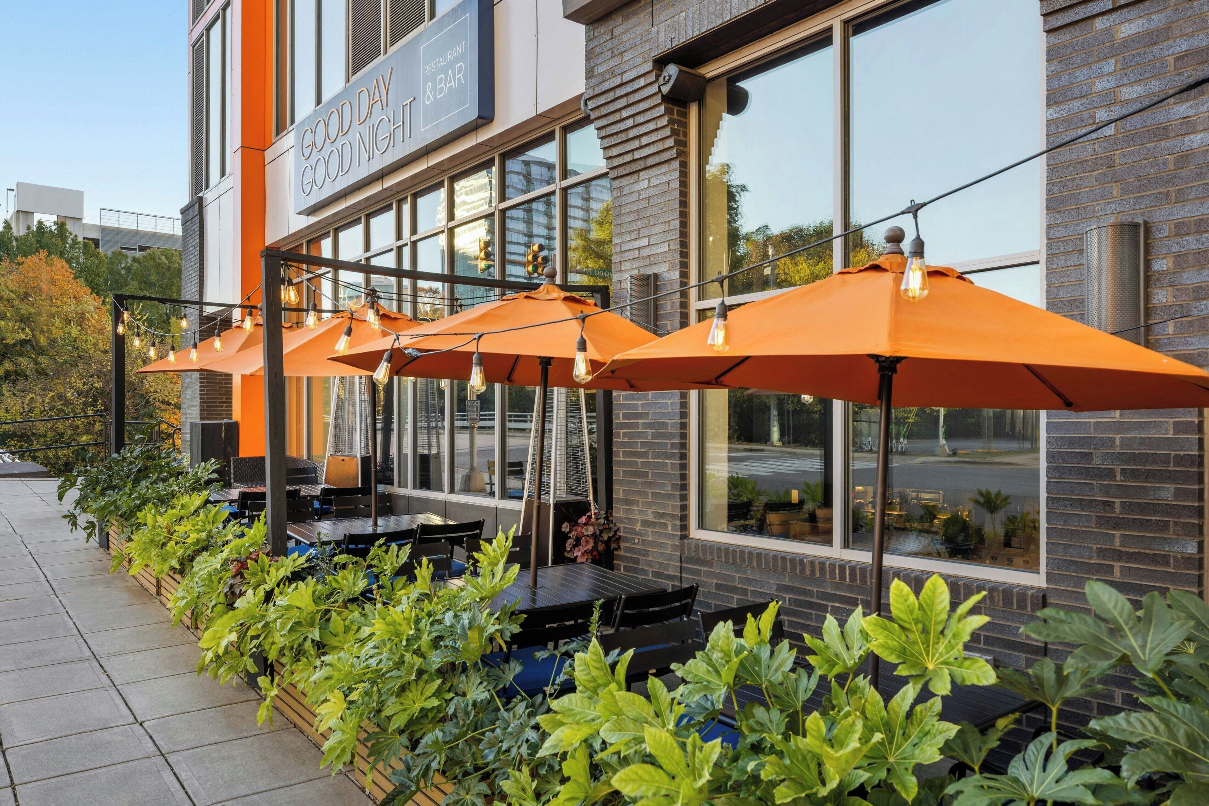 Outdoor seating with orange umbrellas and tables, a brick building facade, and a clear sky.