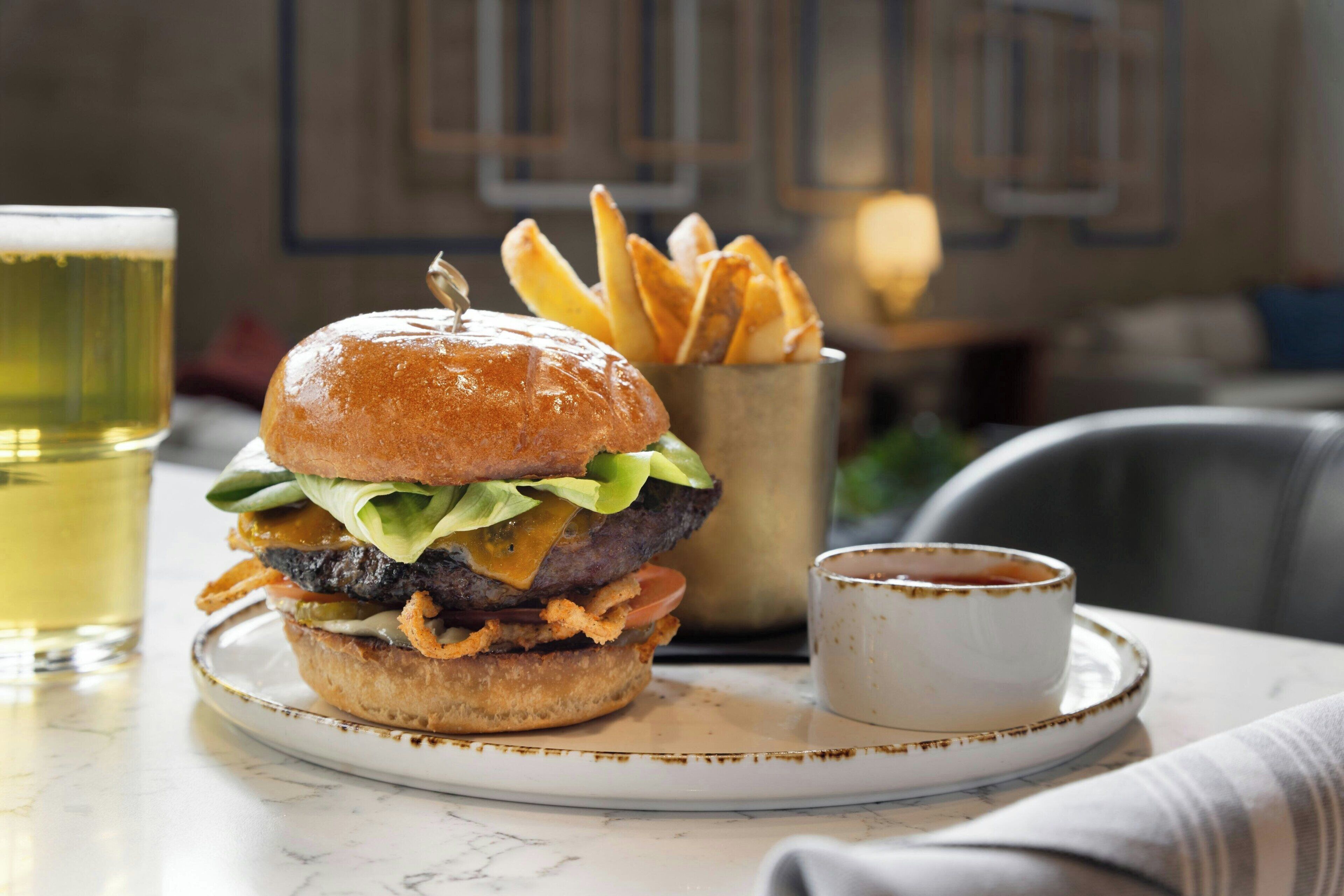 A burger with fries and a cup of sauce on a plate.