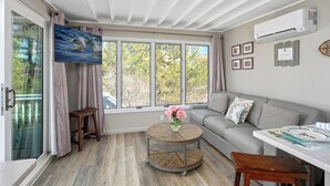 A modern living room with a sofa, a round coffee table with a vase of flowers, a dining table with plates, and a large window with curtains. - 2026 AVAILABLE!PET FRIENDLY 1BR condo OCEANFRONT Building perfect for a COUPLE!! (Long Beach Township)