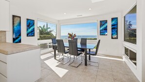 A modern dining area with a large table and chairs, large windows with a view of the ocean, and abstract art on the walls. - Ocean Views, Rooftop Deck, Fire Pit, Game Room, AC (Carlsbad)