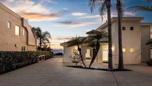 A modern building with a flat roof, large windows, and a paved walkway. - Ocean Views, Rooftop Deck, Fire Pit, Game Room, AC (Carlsbad)