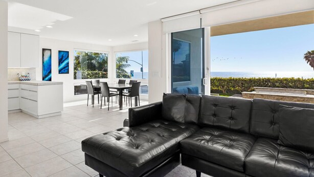 A modern living space with a black leather sofa, a dining area with chairs, and a kitchen with white cabinets. - Ocean Views, Rooftop Deck, Fire Pit, Game Room, AC (Carlsbad)