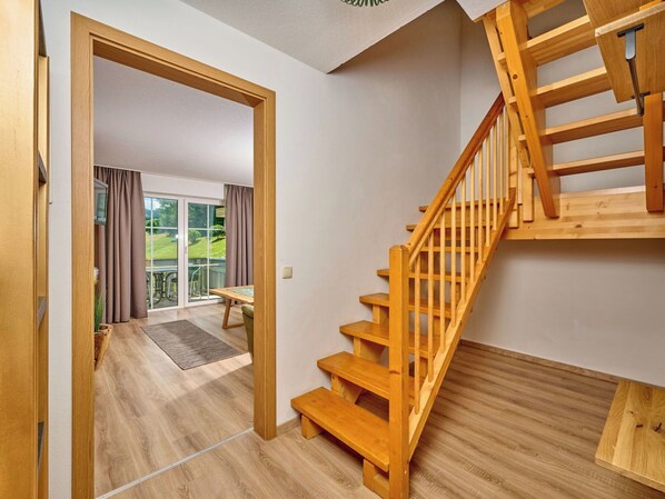 A wooden staircase leading to a balcony with a view of greenery.