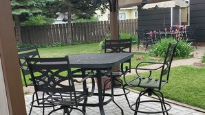 Un patio couvert, agrémenté d’une table et de chaises, entouré d’une clôture en bois et de verdure.